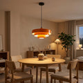 Suspension Bauhaus orange à trois disques empilés, allumée au-dessus d'une table à manger, le soir