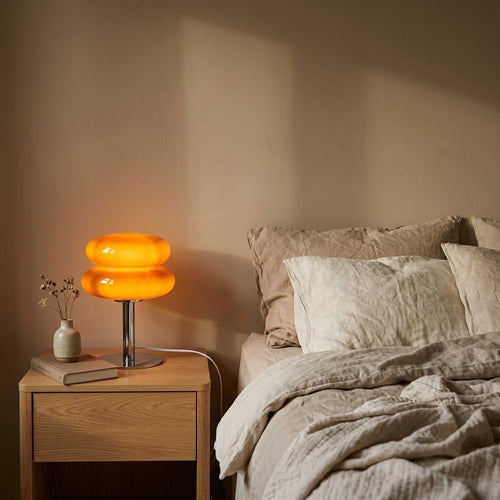 Lampe à poser macaron en verre orange allumée sur une table de chevet, le soir